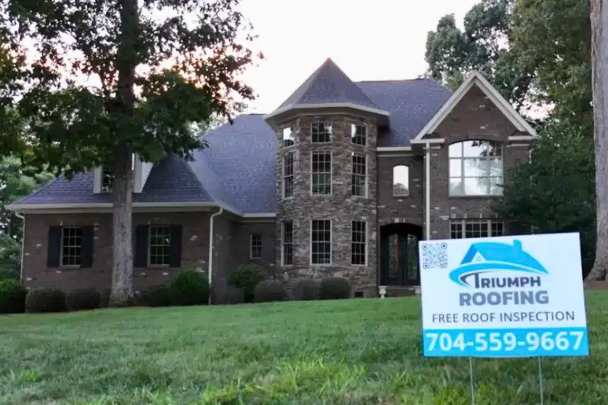A shingle roof replacement on a brick and stone Ballantyne home with a Triumph Roofing yard sign